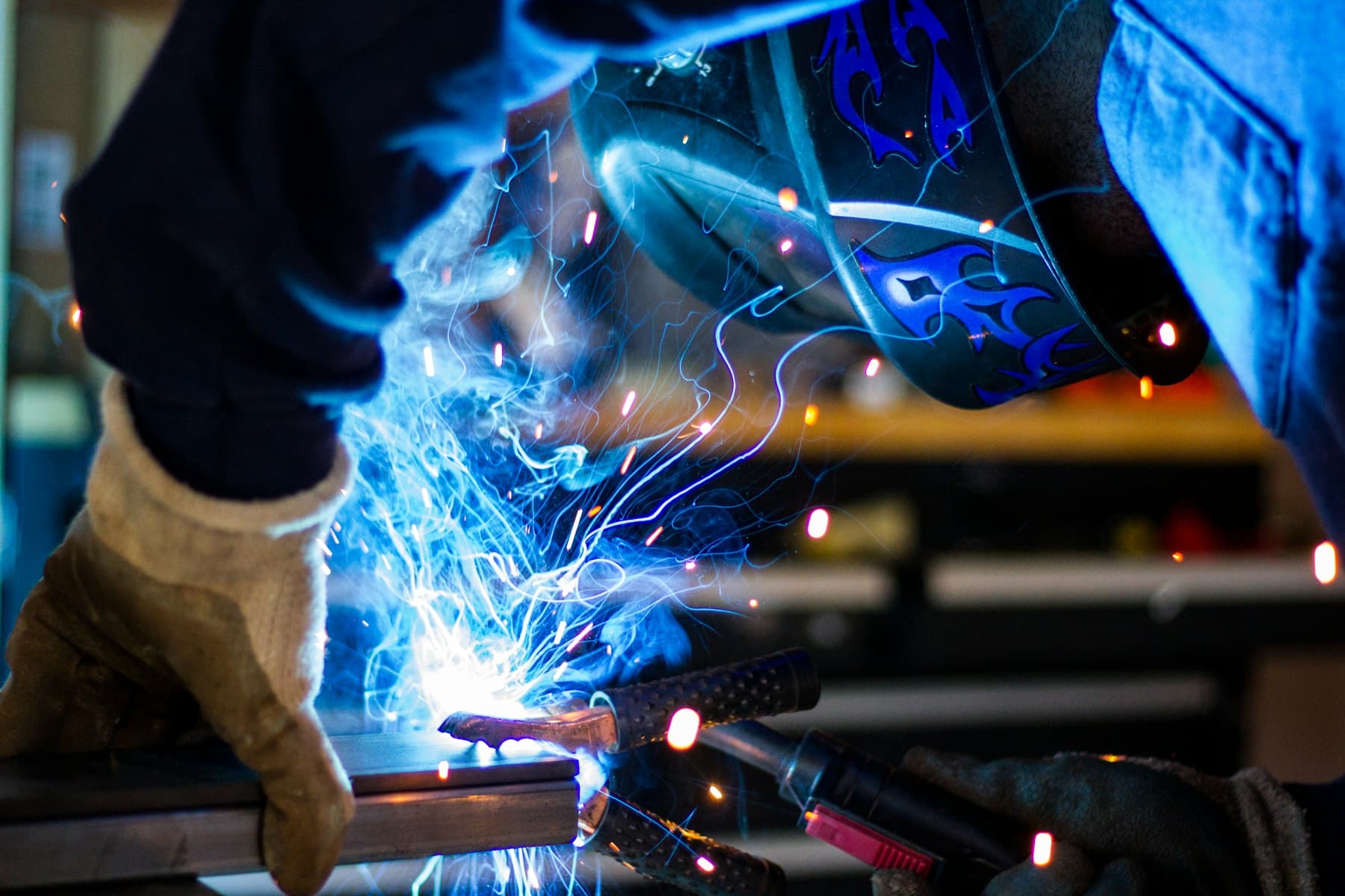 A welder in protective gloves working on metal, with blue sparks