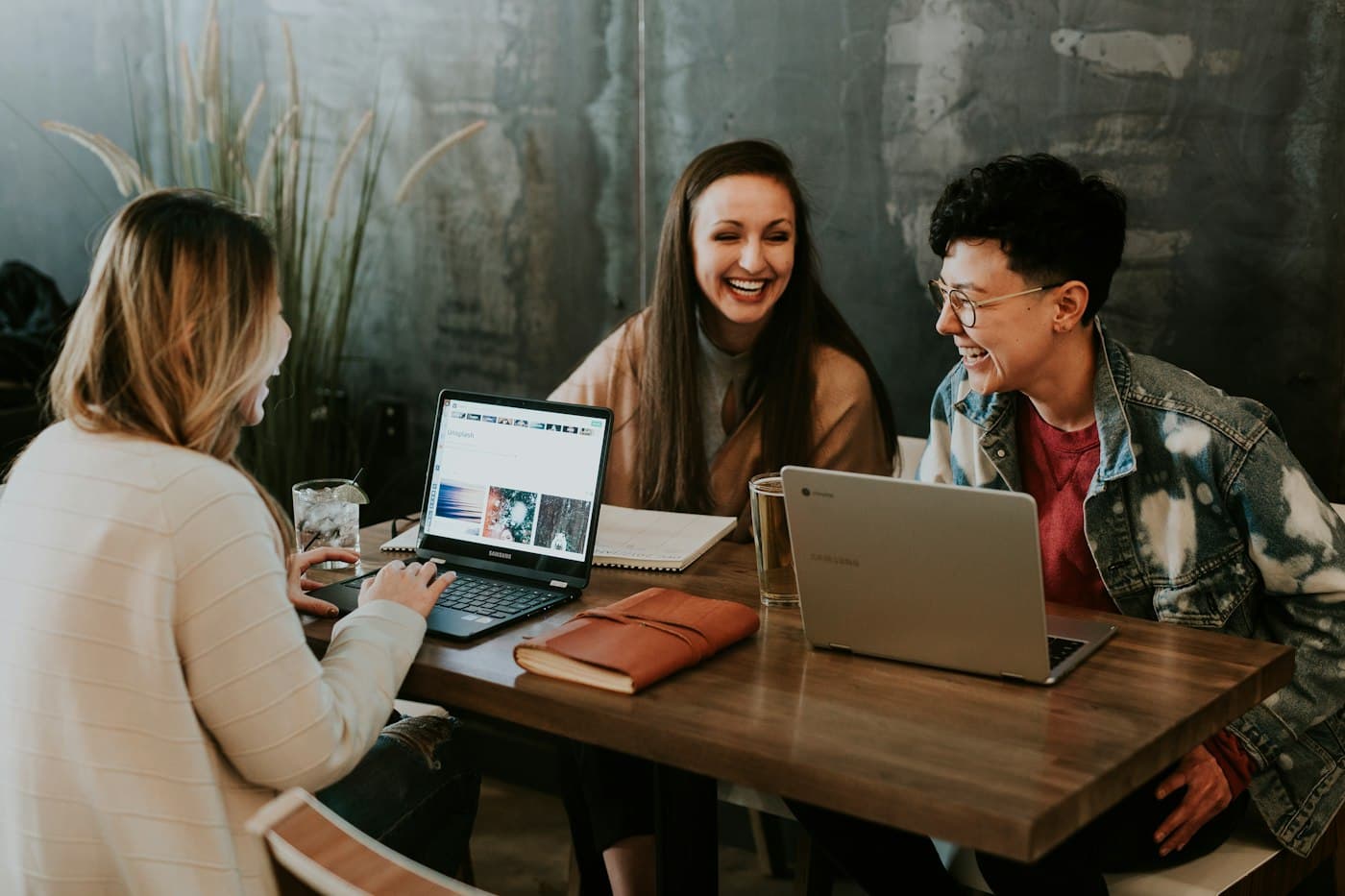 Three students laughing together around a laptop